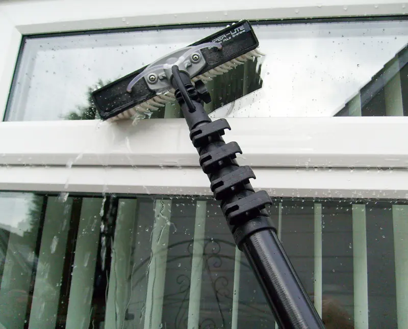 Water-fed pole brush cleaning a white UPVC window